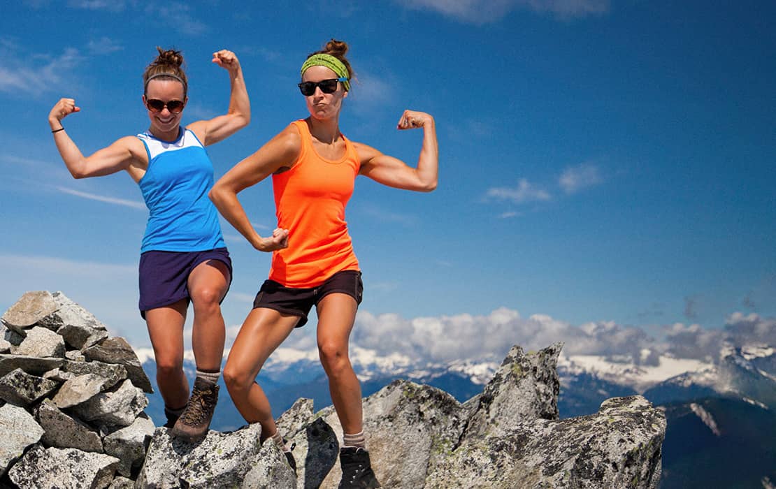 Two women in a bodybuilding pose on top of a mountain